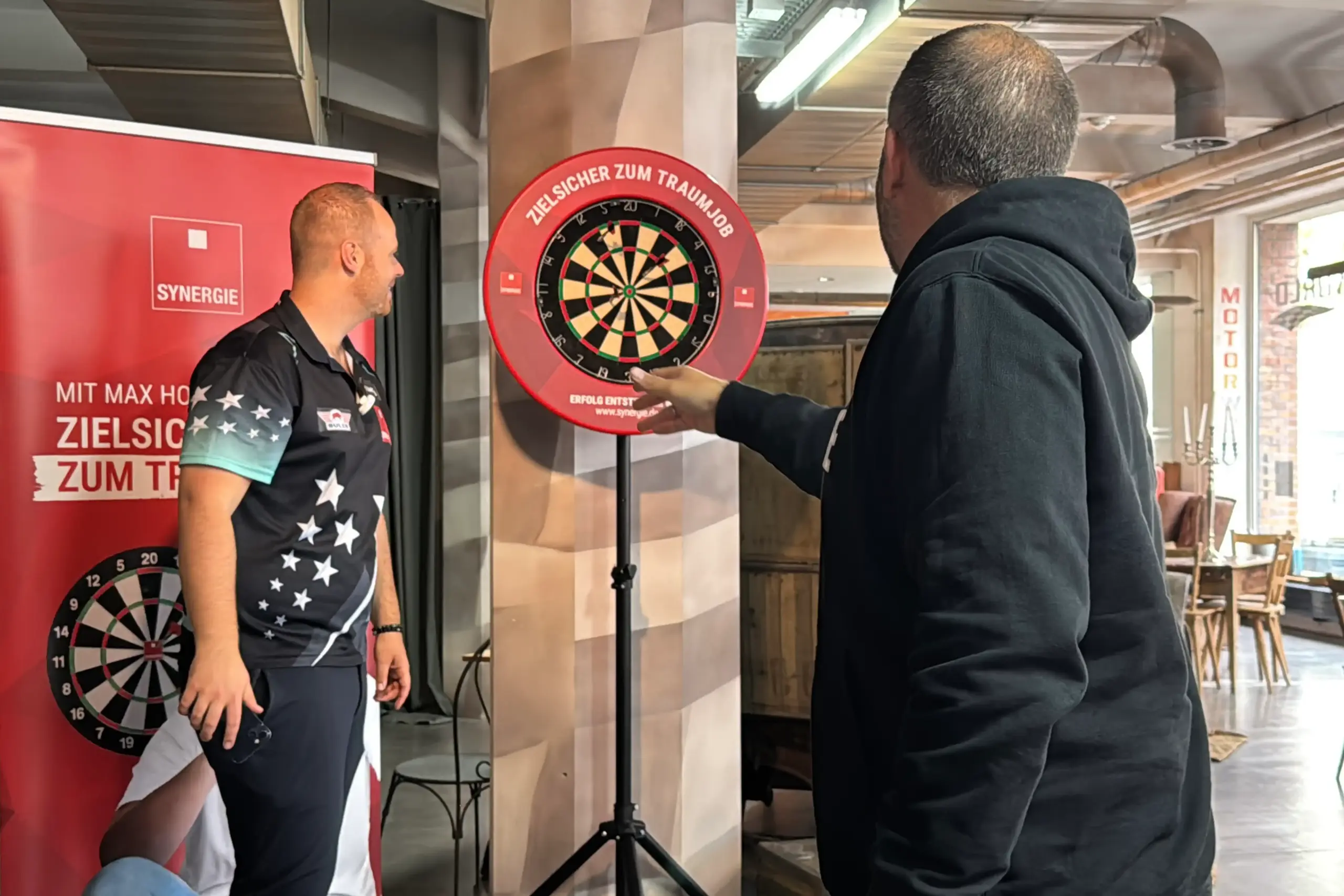 Max Hopp coacht einen Synergiemitarbeiter beim Darts werfen.